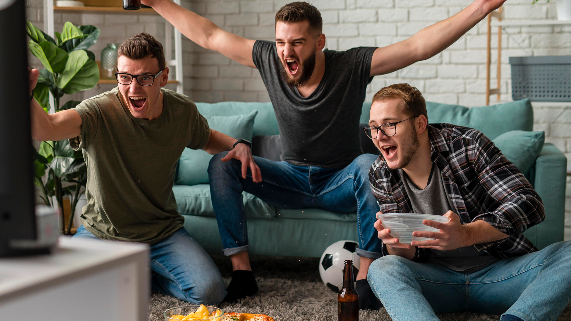 tres homens animados comemorando o gol do seu time 